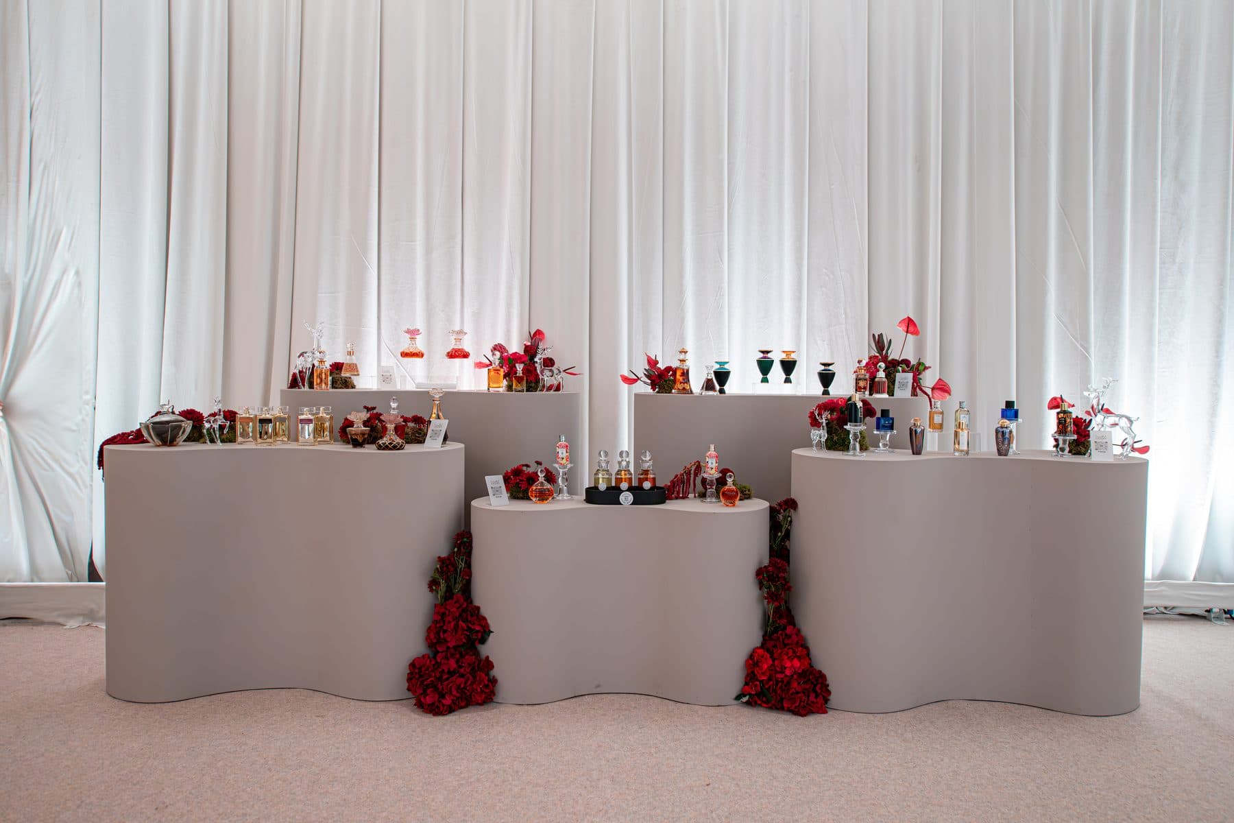 Perfume display with red florals against white drapes